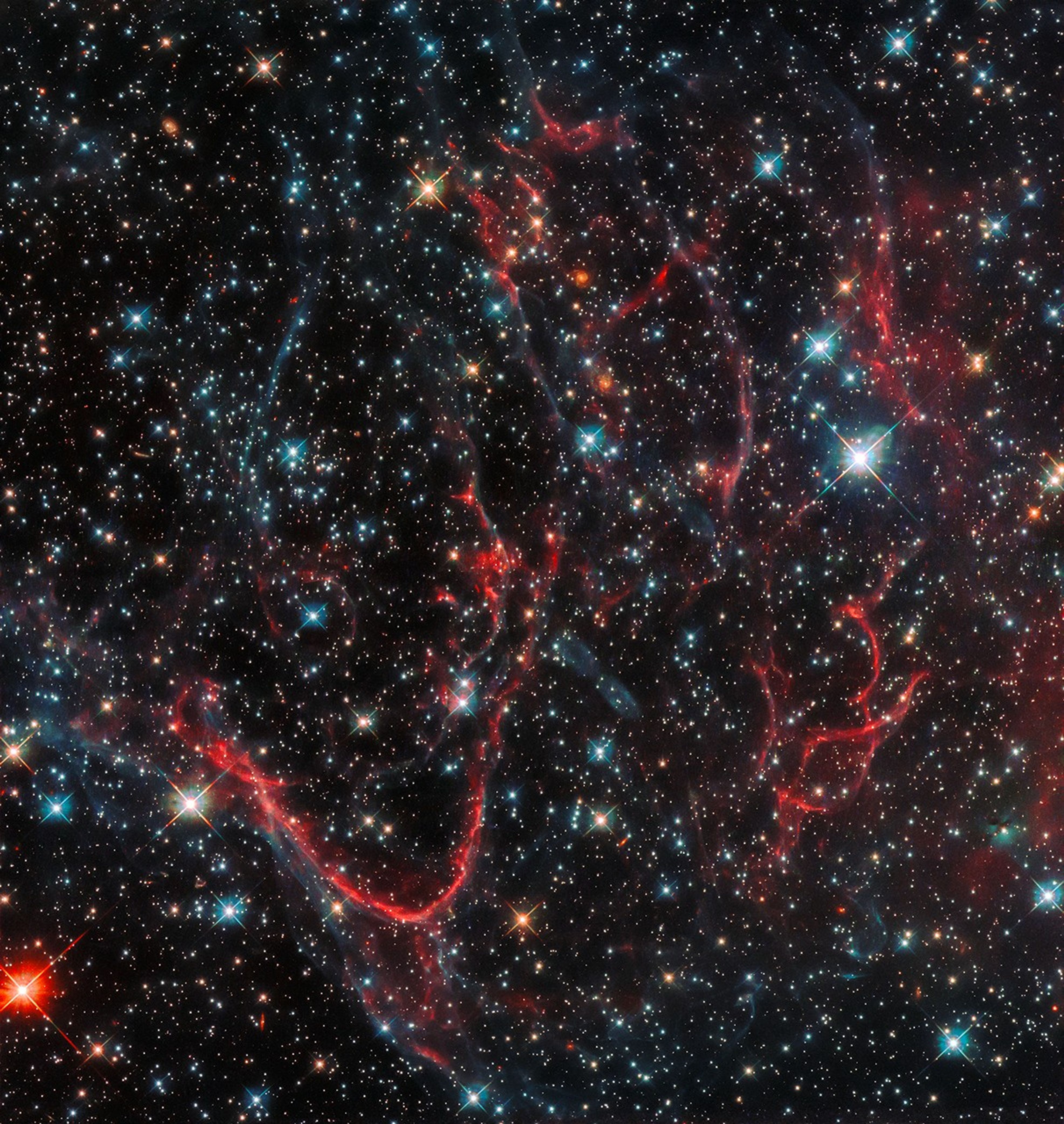 Red and blue streamers of gas and dust in space, with bright multicolored stars scattered throughout.